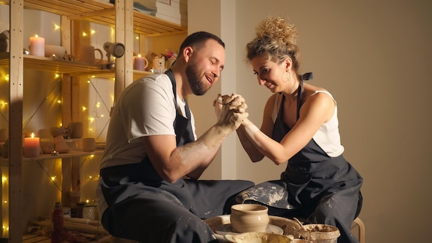 Man en een vrouw die een kleikruik maken op een pottenbakkersschijf. romantisch koppel hand in hand