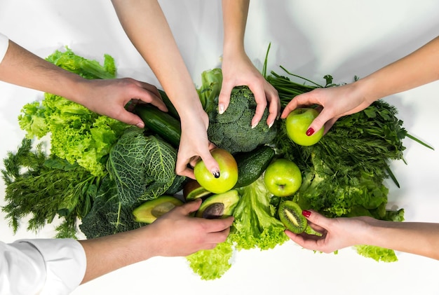 Man en twee vrouwen halen verse groene groenten en fruit van de witte tafel boven een shot rijk voedzaam voedsel