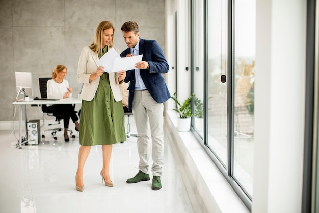 Foto man en vrouw bespreken met papier in handen binnenshuis op kantoor met jonge mensen werkt achter hen