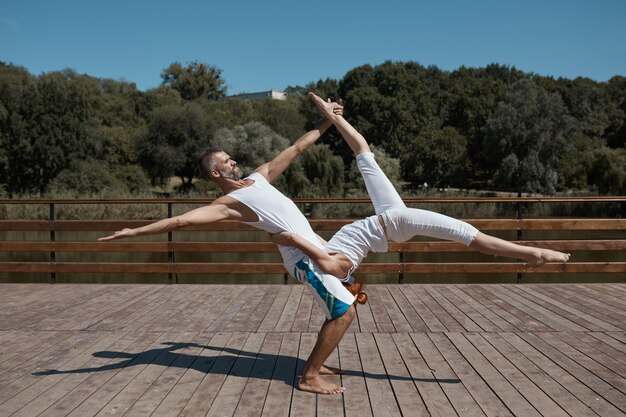 Man en vrouw die in witte kleren geavanceerde yoga in openlucht uitoefenen