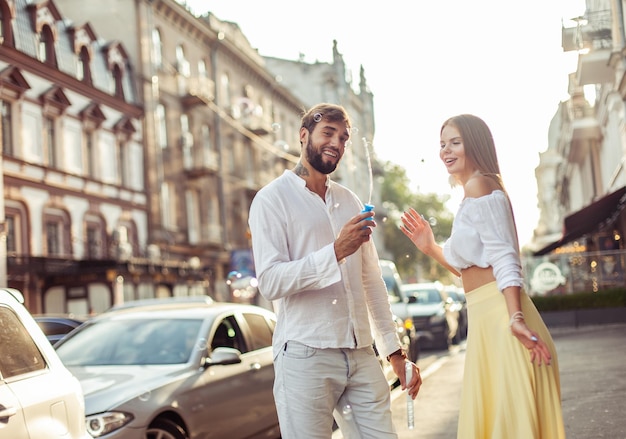 Man en vrouw die plezier hebben met zeepbellen in de stad Jong verliefd stel