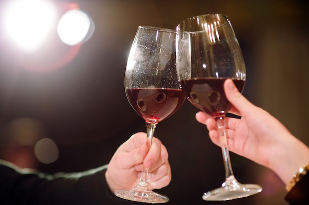 Man en vrouw die rode wijn drinken. Op de foto, close-up handen met een bril.