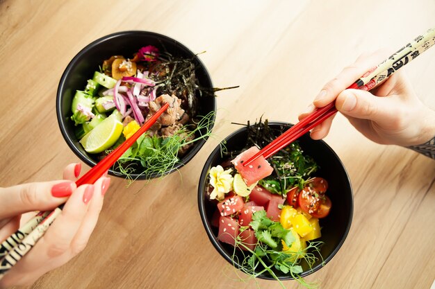 Man en vrouw die zaksalade met eetstokjes eten. schar tonijnsalade in een kom. mensen in het restaurant eten salade met stokjes. aziatische zeevruchten salade concept.