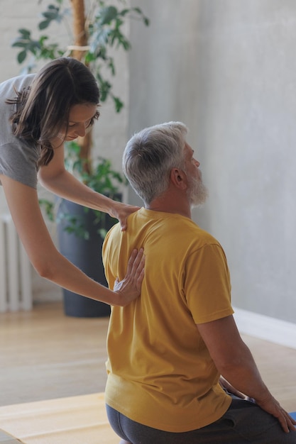 Man en vrouw doen yoga in sportstudio senior coach en jonge volwassen vrouw zorgen voor elkaar