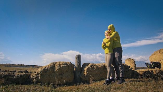 Man en vrouw in geelgroene sportkleding Mooie paar reizigers knuffelen en kussen in de buurt van oude steen genietend van hooglandlandschap Twee reizigers lopen tegen de achtergrond van besneeuwde bergen