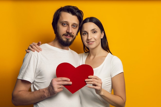 Man en vrouw in witte T-shirts houden op Valentijnsdag een hart van papier vast