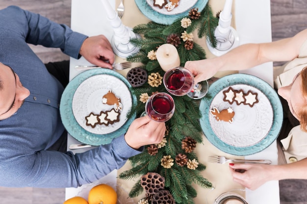 Man en vrouw klinken glazen wijn op kersttafel met koekjes en pijnboomtakken