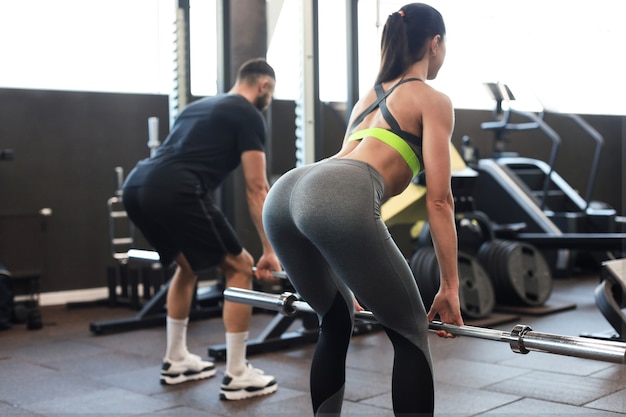 Man en vrouw met barbell buigen spieren in de sportschool.