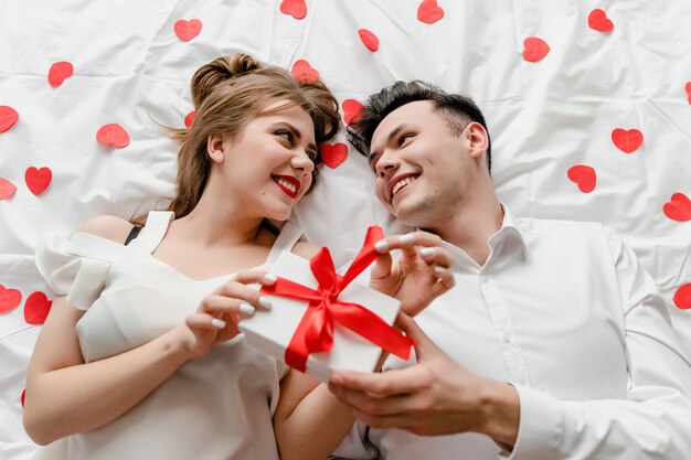 Man en vrouw met cadeau in bed met hartvormige confetti