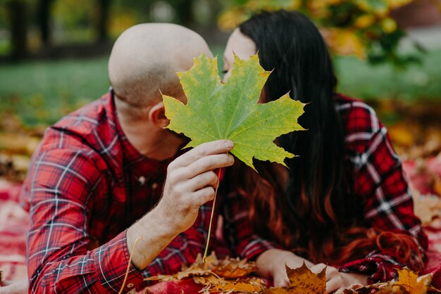 Man en vrouw met een plaid in herfstbladeren en bedekt met een esdoornblad