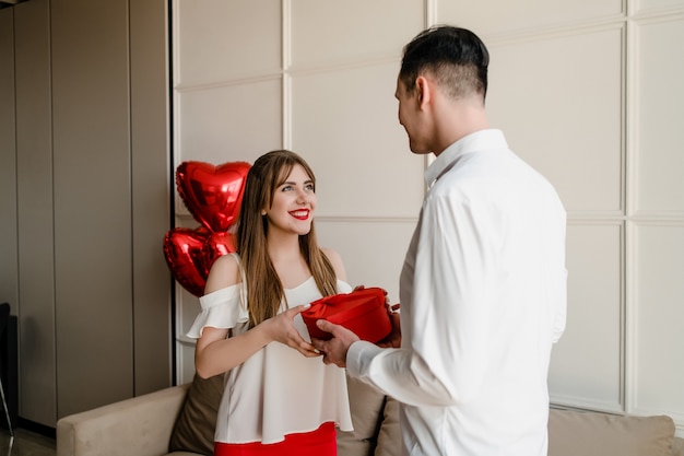 Man en vrouw met hartvormige geschenkdoos en rode ballonnen thuis