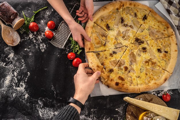 Man en vrouw nemen plakjes heerlijke kaas pizza uit zwarte tafelblad weergave