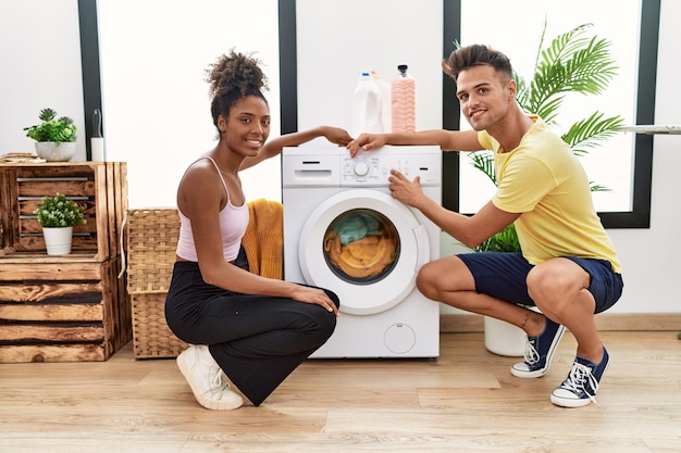 Man en vrouw paar glimlachend zelfverzekerd zetten wasmachine aan in wasruimte