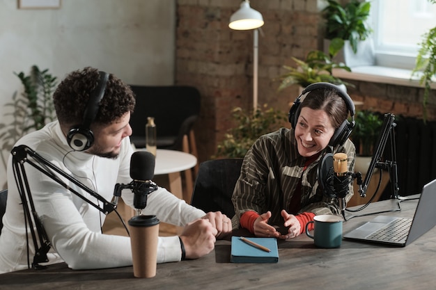 Man en vrouw praten met elkaar terwijl ze aan tafel zitten met microfoons en aan de radio werken