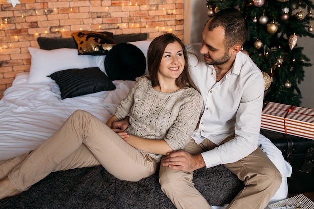 Man en vrouw thuis dichtbij Kerstboom. Verliefde paar op bed