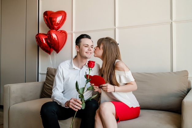 Man en vrouw thuis op de bank met rode roos en hartvormige valentijn kaart