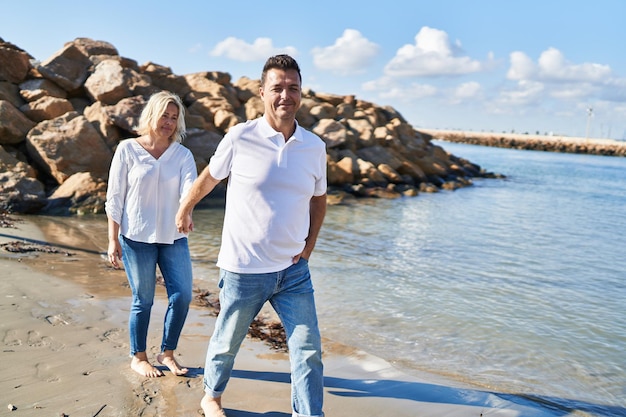 Man en vrouw van middelbare leeftijd paar glimlachend zelfverzekerd wandelen aan zee