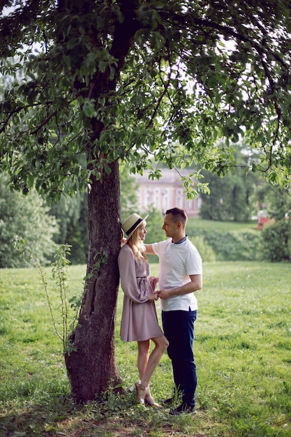 Man en vrouw verliefd in een jurk en hoed staan in de zomer op een groen veld onder een boom