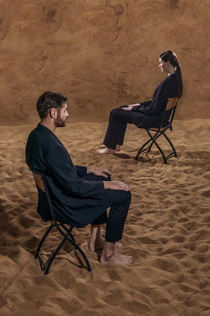 Man en vrouw zitten op de stoelen op de zandcyclorama en kijken in verschillende richtingen.