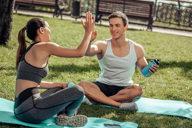 Man en vrouw zitten op matten in het park en geven high five na buiten trainen