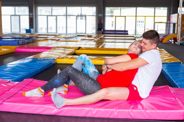 Man en vrouw zitten samen op een trampoline binnenshuis.