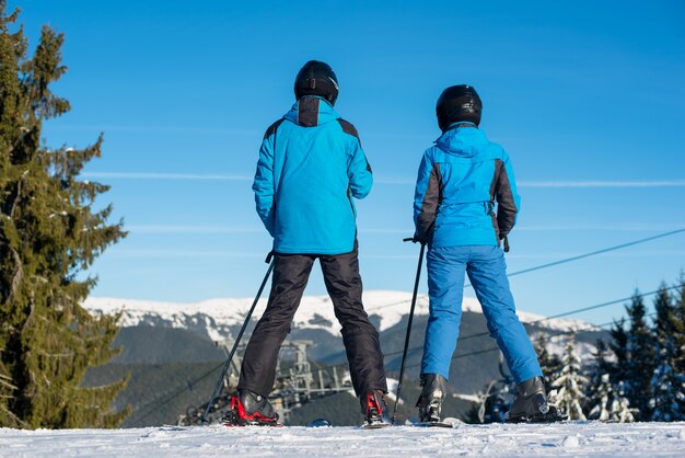 Man en vrouwenskiërs die zich op bergbovenkant bevinden die samen van mooi berglandschap op een de wintertoevlucht genieten bij zonnige dag