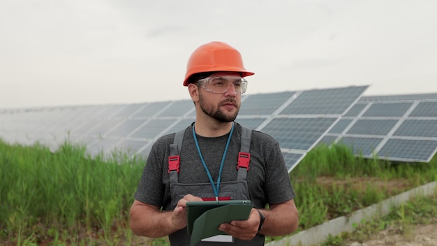 Man engineer in uniform hold digital tablet and working near solar panels power farm. Solar panel field. Clean energy production. Green energy.