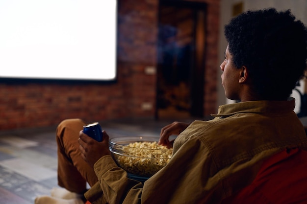 Man enjoy watching film using video projector. Young guy rest eating popcorn drinking soda