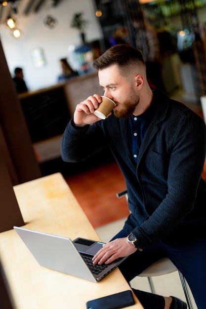 Man enjoying a cup of coffee while working on his laptop A man drinking coffee while using a laptop