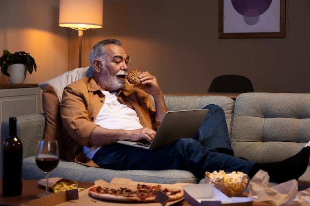 Man enjoying his home alone time with food and wine while using laptop