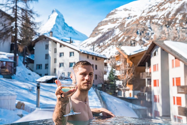 冬の間にマッターホルン山と家に対してプールでワインを楽しむ男