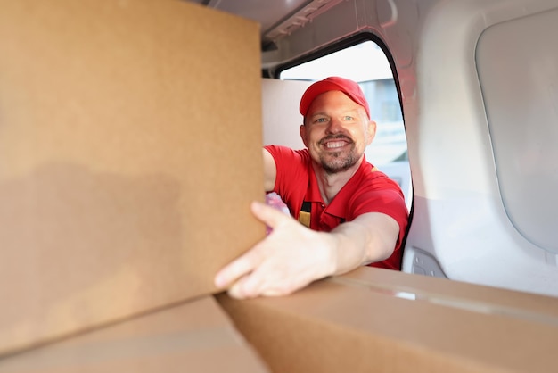 Foto l'uomo che si diverte a lavorare in una società di consegne mette le scatole nel camion per ulteriori consegne all'indirizzo