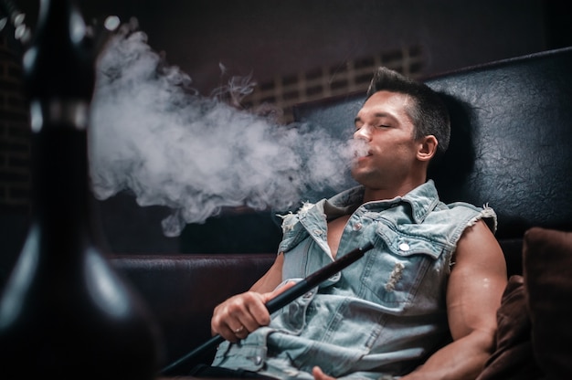 A man of European appearance smokes a fragrant oriental hookah in nightclub