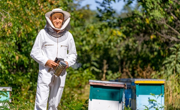 Man examining hives in summer Agricultural beekeeper in protective cloth posing for camera