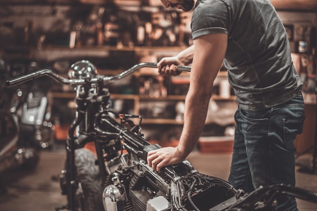 Photo man examining motorcycle. close-up of young man examining motorcycle in repair shop