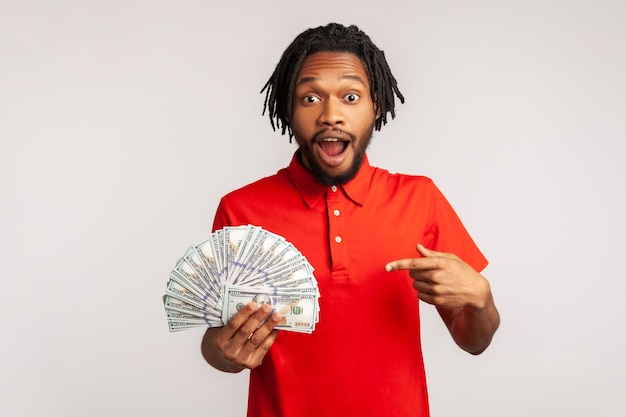 Man excited and surprised to have money, pointing at dollar bills in hand, shocked by lottery win.