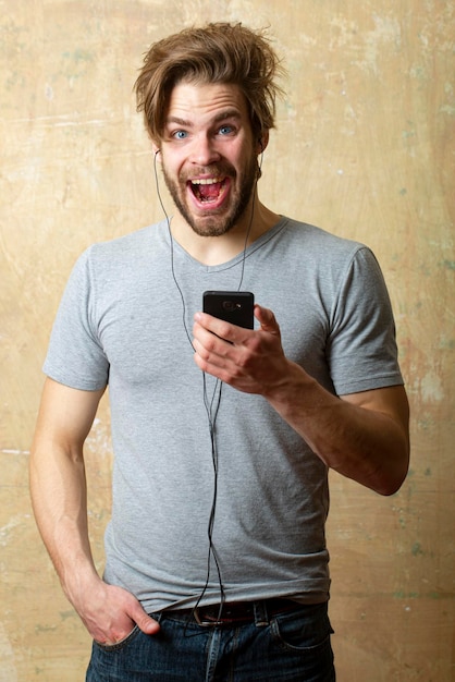 Man excited with smartphone listening music surprised male with phone and earphones emotional portra