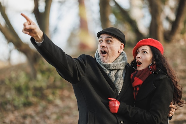 Фото Мужчина, возбужденно указывающий на что-то, и женщина, выражающая удивление, в парке