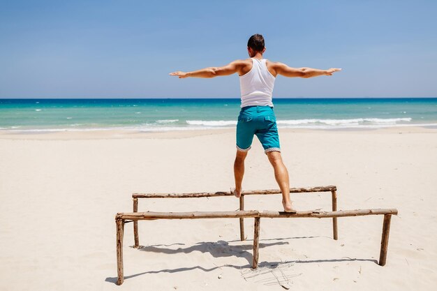 写真 青い空を背景にビーチで平行バーで運動する男性