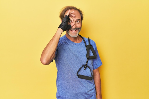 Man exercising with bands in studio excited keeping ok gesture on eye