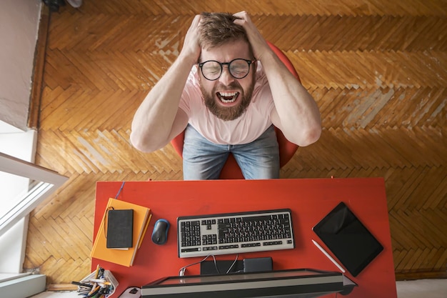 Man experiences stress remotely working at home on computer he grabs hands on head and screams