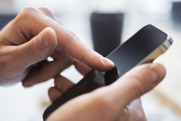 Man expertly using a cuttingedge smartphone at his workspace laptop on standby against the vague backdrop of a thriving office