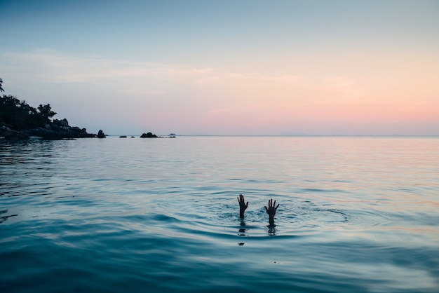 Man exploring the depth of the sea on sunset. Dive under the water and show hands on the surface..