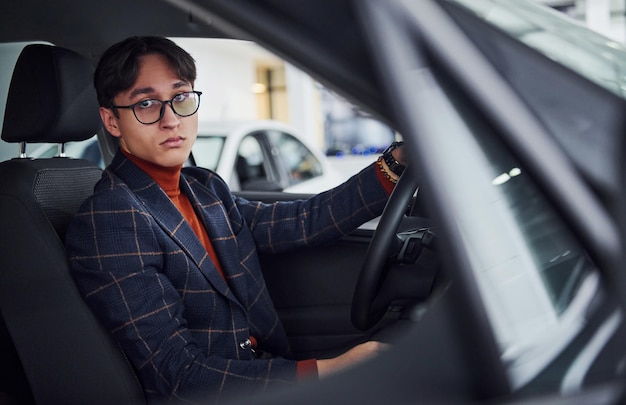 Man in eyewear and formal clothes sitting inside of modern car.