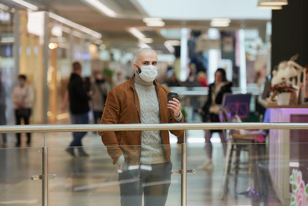 A man in a face mask to avoid the spread of coronavirus is\
holding a cup of coffee in the shopping