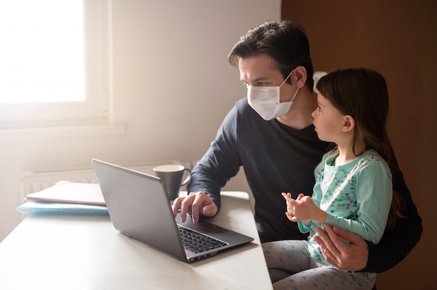 Man in face mask and his little daughter using laptop