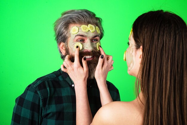 Foto cetriolo facciale dell'uomo. coppia divertente con una maschera di argilla. modello maschile barbuto e modello femminile con maschera di argilla sul viso.