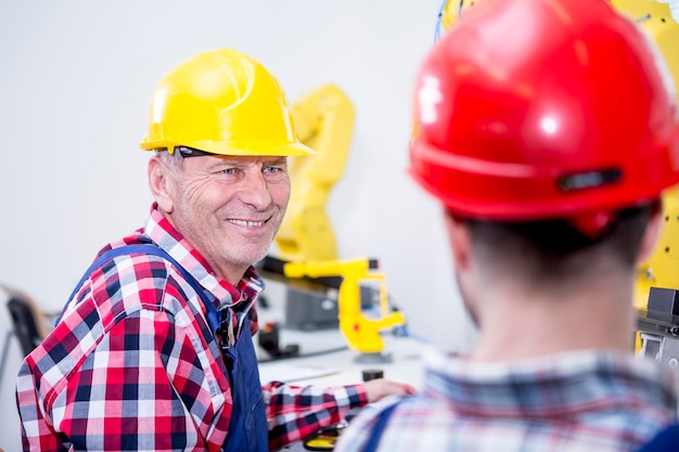 Man in factory wearing hard hat smiling at colleague