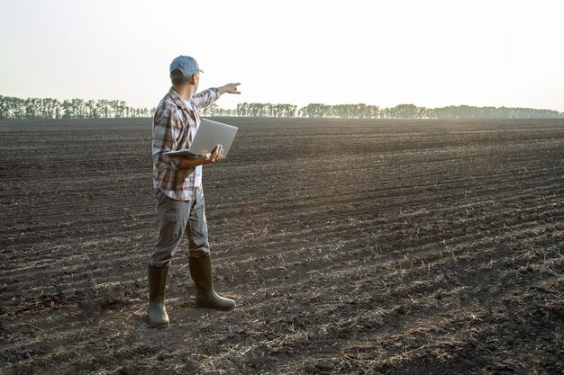 Мужчина-фермер работает на своем ноутбуке в поле, планируя сельское хозяйство Инновации в агробизнесе