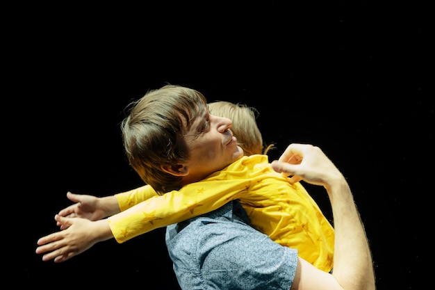 Man father dad holds little kid boy son six years old in his arms and hugs happy family parenthood fatherhood and childhood in studio illuminated by white yellow bright light and black background